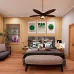 Modern cottage bedroom with patterned yellow wallpaper, green geometric wall art, a grey upholstered bed, and a small sitting area by the window